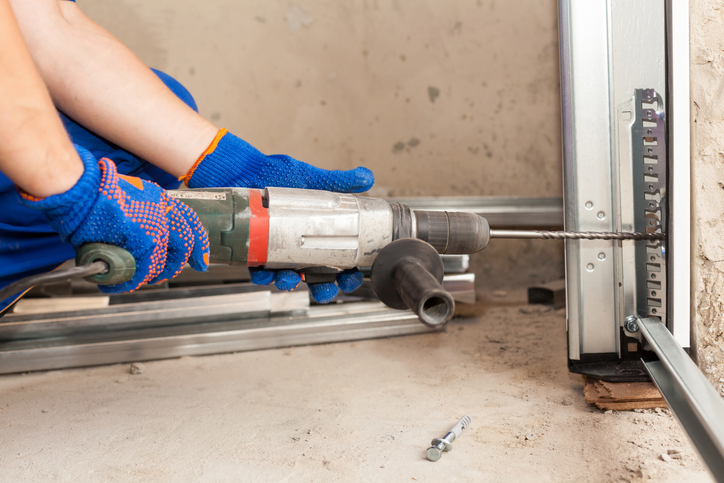 Garage doors installation. Worker drills a hole for the bolt